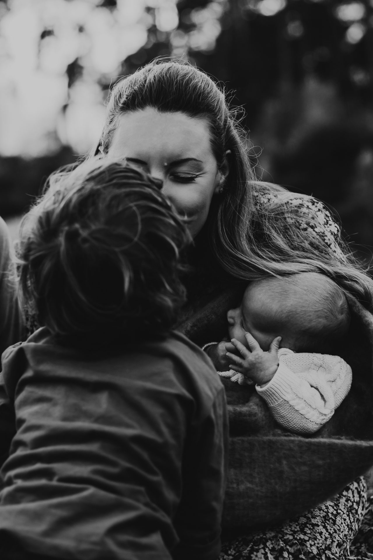 black and white photo of mum kissing her boy toddler and holding newborn